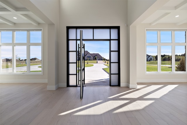 foyer entrance featuring coffered ceiling, light wood-type flooring, beamed ceiling, and a wealth of natural light