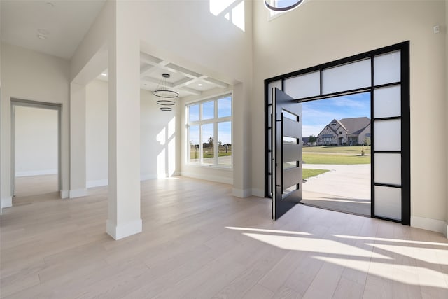 entryway featuring beamed ceiling, coffered ceiling, an inviting chandelier, and light wood-type flooring