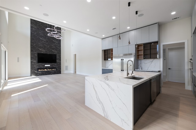 kitchen featuring light hardwood / wood-style floors, pendant lighting, sink, light stone counters, and a spacious island