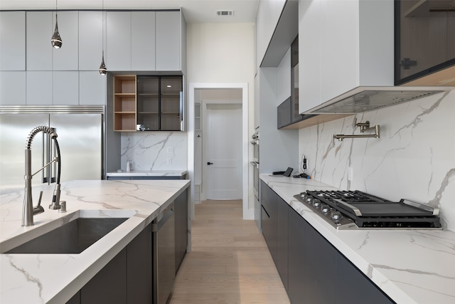 kitchen featuring pendant lighting, light hardwood / wood-style flooring, sink, light stone countertops, and white cabinets