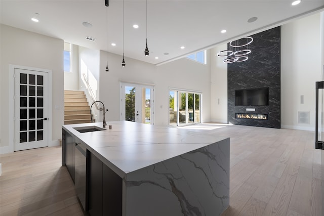 kitchen featuring an island with sink, sink, decorative light fixtures, light wood-type flooring, and a towering ceiling