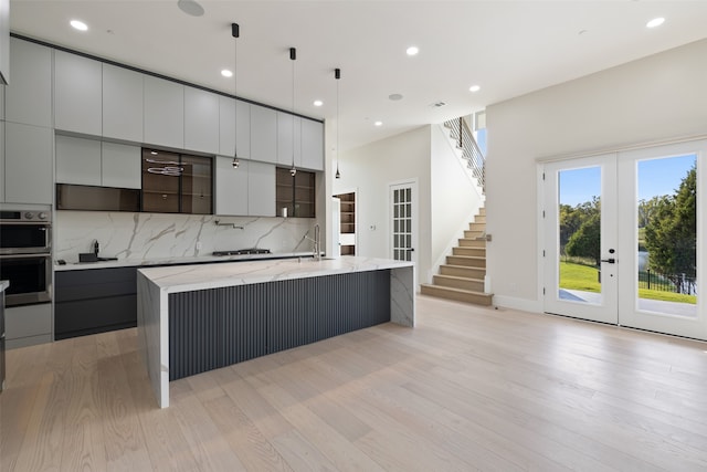 kitchen with light hardwood / wood-style flooring, french doors, a large island with sink, light stone countertops, and hanging light fixtures