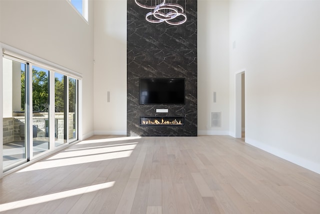 unfurnished living room featuring a premium fireplace, a towering ceiling, and light hardwood / wood-style floors