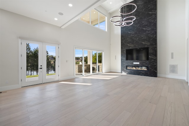 unfurnished living room featuring a towering ceiling, french doors, light hardwood / wood-style flooring, and a fireplace