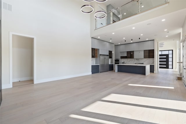 unfurnished living room with a high ceiling, light hardwood / wood-style flooring, and sink