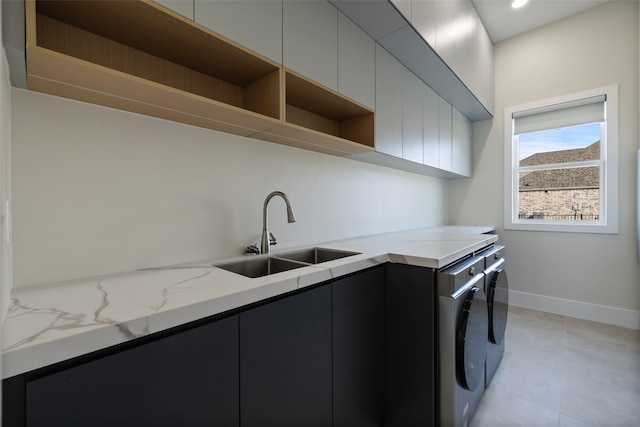 clothes washing area with washer and clothes dryer, sink, light tile patterned floors, and cabinets