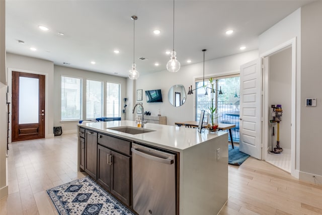 kitchen featuring sink, dishwasher, light hardwood / wood-style floors, pendant lighting, and a kitchen island with sink