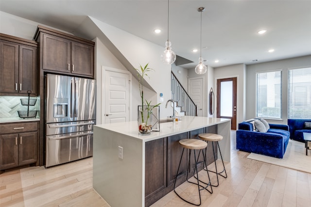 kitchen with a center island with sink, stainless steel fridge with ice dispenser, light hardwood / wood-style flooring, and tasteful backsplash