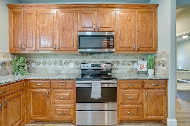 kitchen with light wood-type flooring, backsplash, stainless steel appliances, and light stone counters