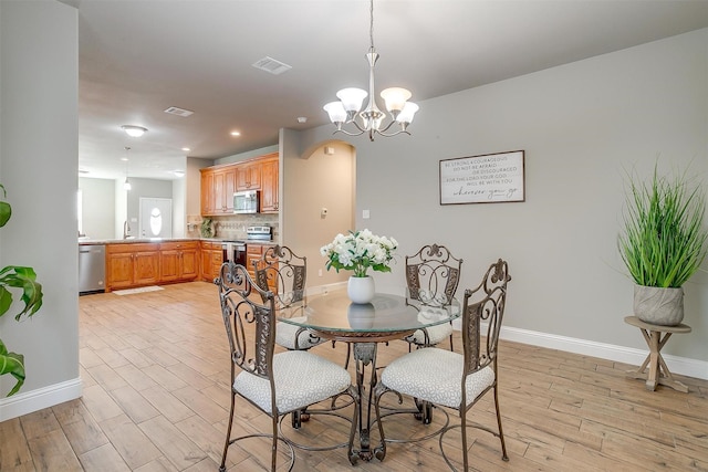 dining space with an inviting chandelier, sink, and light hardwood / wood-style flooring