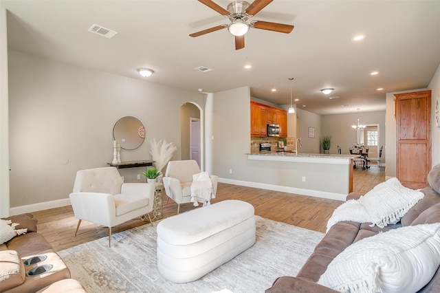 living room featuring ceiling fan with notable chandelier and light wood-type flooring