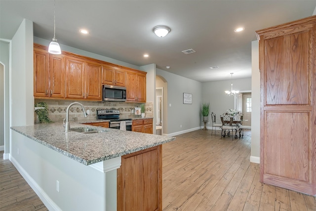 kitchen with sink, hanging light fixtures, stainless steel appliances, light stone counters, and light hardwood / wood-style floors