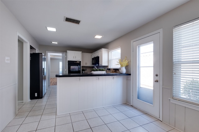 kitchen featuring white cabinets, kitchen peninsula, black appliances, and light tile patterned flooring