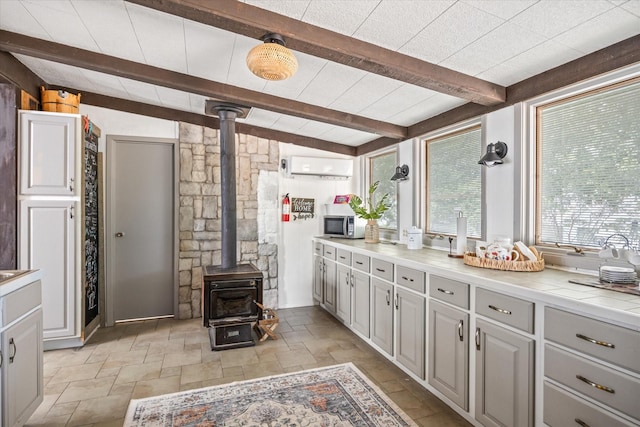 kitchen featuring tile counters, stainless steel microwave, a wood stove, stone tile flooring, and an AC wall unit