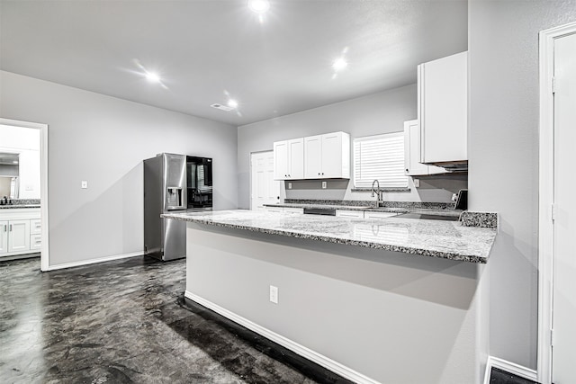 kitchen with light stone countertops, kitchen peninsula, sink, stainless steel fridge with ice dispenser, and white cabinetry