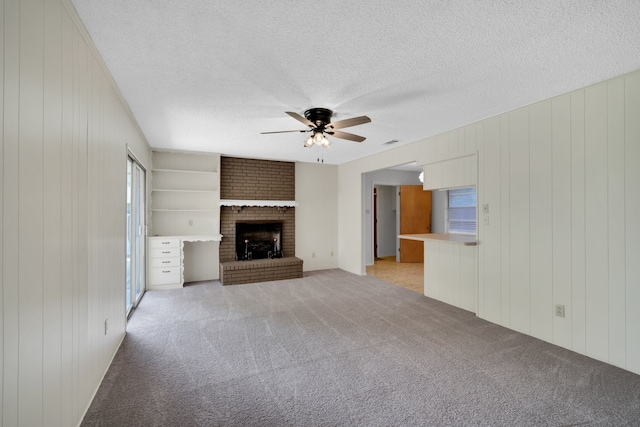 unfurnished living room with ceiling fan, carpet flooring, a textured ceiling, and a fireplace