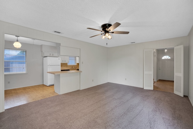 unfurnished living room featuring a textured ceiling, ceiling fan, and light colored carpet