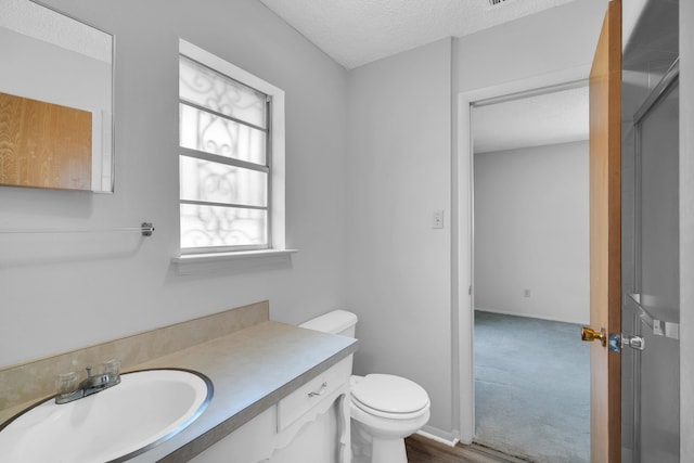 bathroom with hardwood / wood-style flooring, vanity, a textured ceiling, toilet, and a shower with door