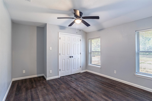 unfurnished bedroom with ceiling fan, a closet, dark wood-type flooring, and multiple windows