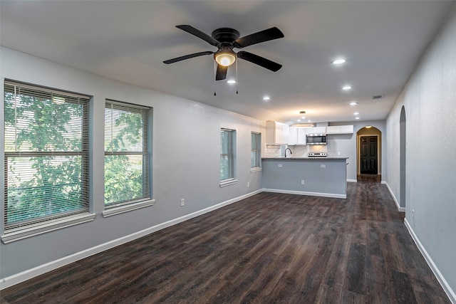 unfurnished living room featuring ceiling fan, a healthy amount of sunlight, and dark hardwood / wood-style flooring