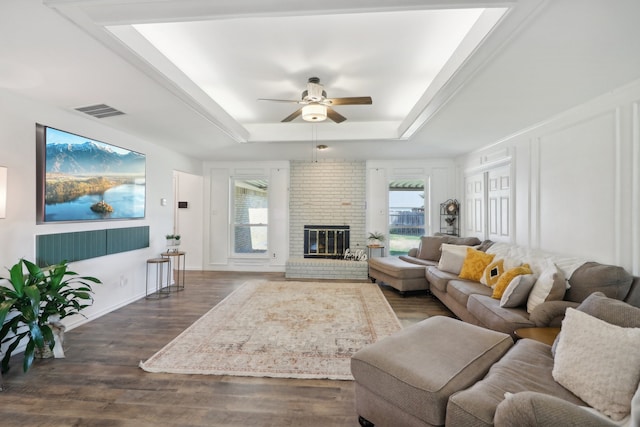 living room featuring ceiling fan, a healthy amount of sunlight, dark hardwood / wood-style flooring, a tray ceiling, and a fireplace