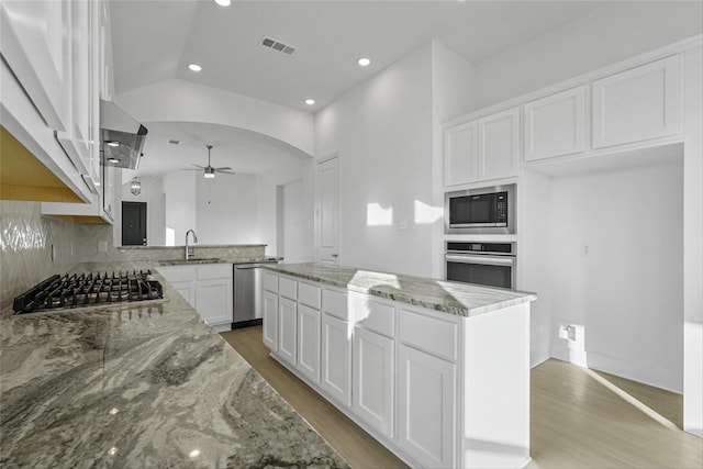 kitchen with light stone countertops, appliances with stainless steel finishes, backsplash, a kitchen island, and white cabinetry