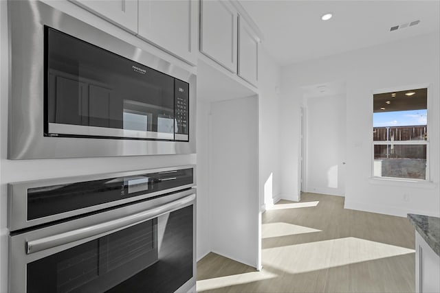 kitchen with white cabinets, light wood-type flooring, stone countertops, and appliances with stainless steel finishes