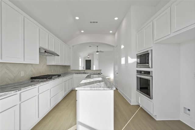 kitchen with a center island, stainless steel appliances, light stone counters, backsplash, and vaulted ceiling