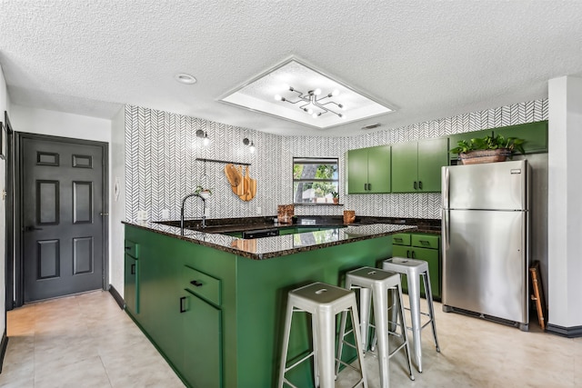 kitchen with green cabinets, stainless steel refrigerator, kitchen peninsula, a breakfast bar, and a textured ceiling