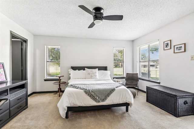 bedroom with ceiling fan, light colored carpet, and a textured ceiling