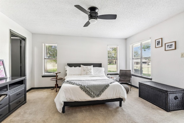 bedroom with a ceiling fan, light colored carpet, a textured ceiling, and baseboards