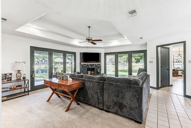 living room featuring a fireplace, a tray ceiling, light tile patterned flooring, ceiling fan, and a textured ceiling