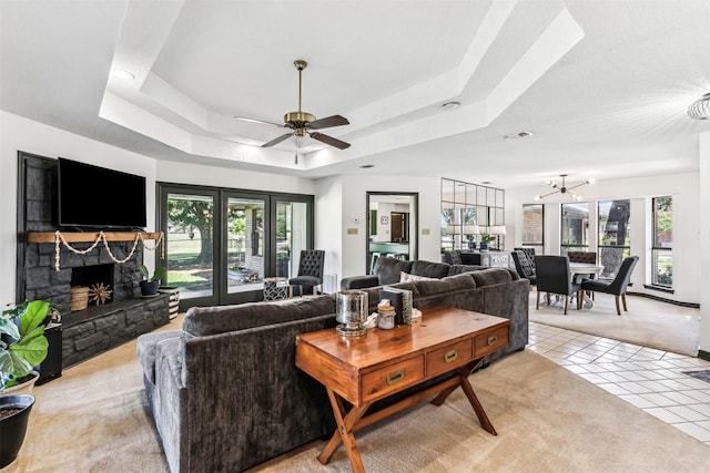 living room featuring light tile patterned floors, a raised ceiling, a wealth of natural light, and a stone fireplace