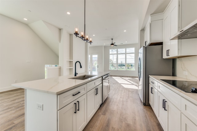 kitchen featuring light wood-type flooring, ceiling fan with notable chandelier, a kitchen island with sink, black electric cooktop, and sink