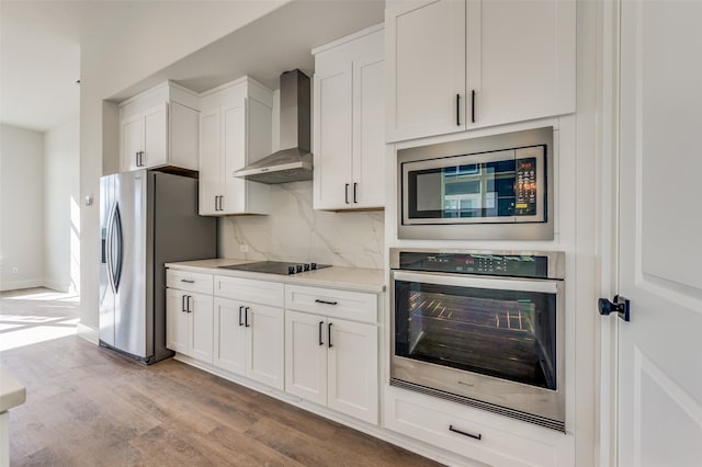 kitchen with wall chimney range hood, backsplash, white cabinets, light hardwood / wood-style floors, and stainless steel appliances