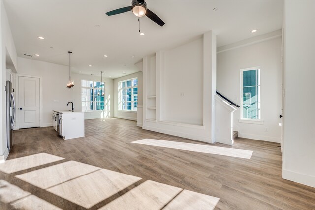 unfurnished living room featuring sink, light hardwood / wood-style floors, and ceiling fan with notable chandelier