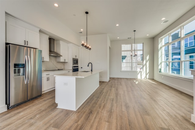 kitchen with an inviting chandelier, light wood-type flooring, appliances with stainless steel finishes, decorative backsplash, and wall chimney range hood