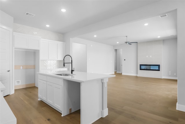 kitchen with a kitchen island with sink, sink, light hardwood / wood-style floors, and white cabinets