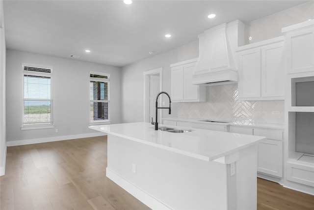 kitchen featuring custom exhaust hood, an island with sink, sink, light hardwood / wood-style flooring, and white cabinetry