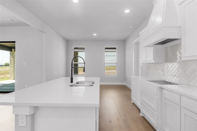 kitchen featuring sink, light hardwood / wood-style floors, white cabinetry, custom exhaust hood, and a center island with sink