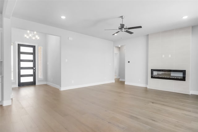 unfurnished living room featuring ceiling fan with notable chandelier, a fireplace, and light hardwood / wood-style flooring