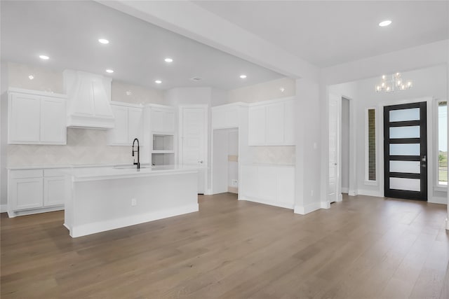 kitchen with an island with sink, decorative backsplash, hardwood / wood-style floors, white cabinets, and sink