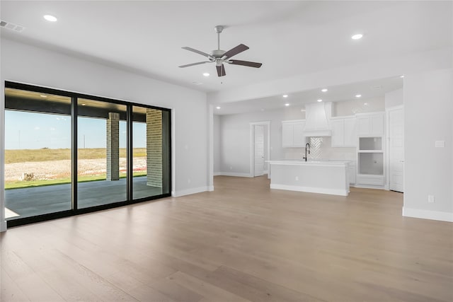 unfurnished living room with light hardwood / wood-style floors, sink, and ceiling fan