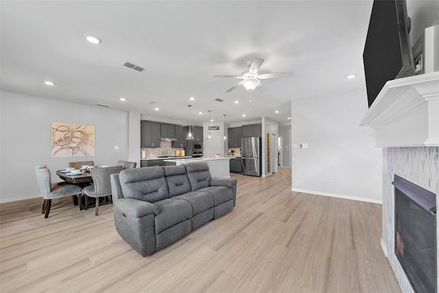 living room with ceiling fan, light wood-type flooring, and a fireplace