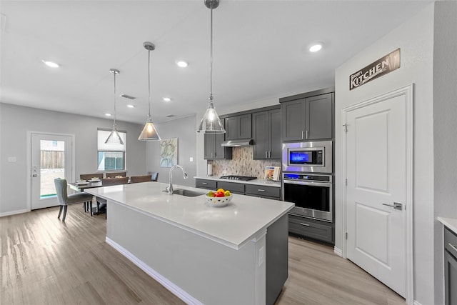 kitchen featuring sink, stainless steel appliances, light hardwood / wood-style floors, decorative light fixtures, and a kitchen island with sink