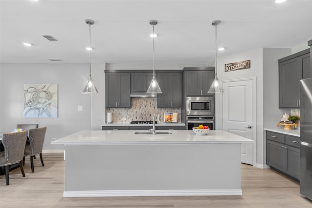 kitchen featuring sink, light hardwood / wood-style flooring, an island with sink, decorative light fixtures, and stainless steel appliances