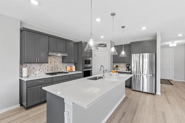 kitchen with backsplash, a kitchen island with sink, sink, decorative light fixtures, and stainless steel appliances