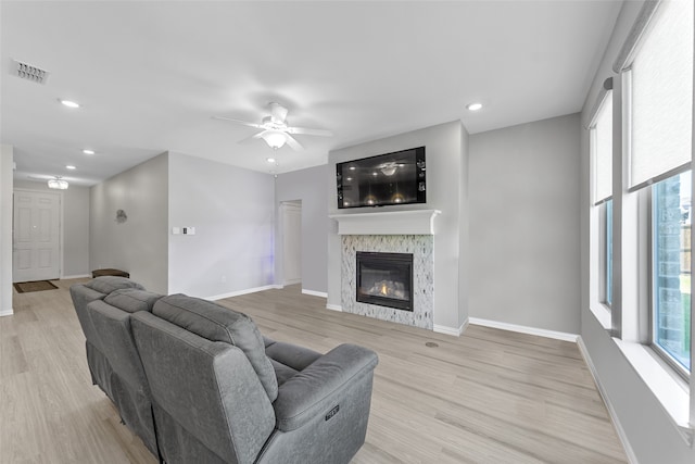 living room featuring a stone fireplace, ceiling fan, and light hardwood / wood-style flooring