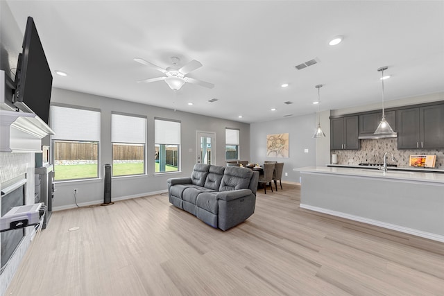 living room with ceiling fan, light wood-type flooring, and a tile fireplace