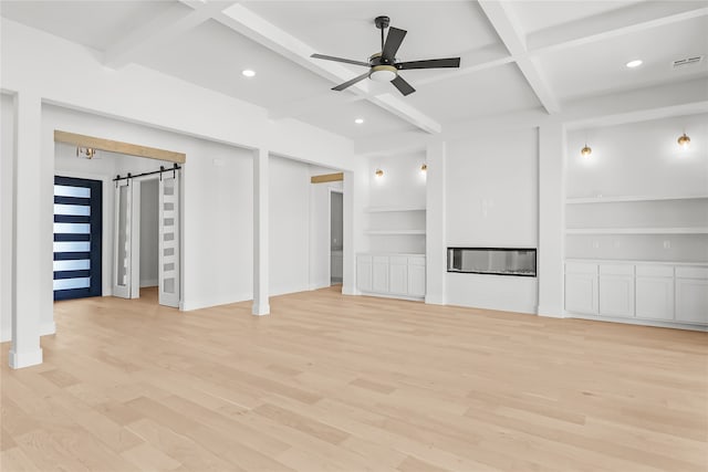 unfurnished living room featuring ceiling fan, a barn door, light wood-type flooring, beamed ceiling, and coffered ceiling